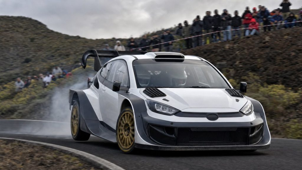 Coche de rally de la máxima categoría saliendo de una horquilla de asfalto en una carretera de montaña con público en las cunetas