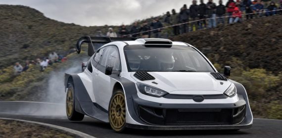 Coche de rally de la máxima categoría saliendo de una horquilla de asfalto en una carretera de montaña con público en las cunetas