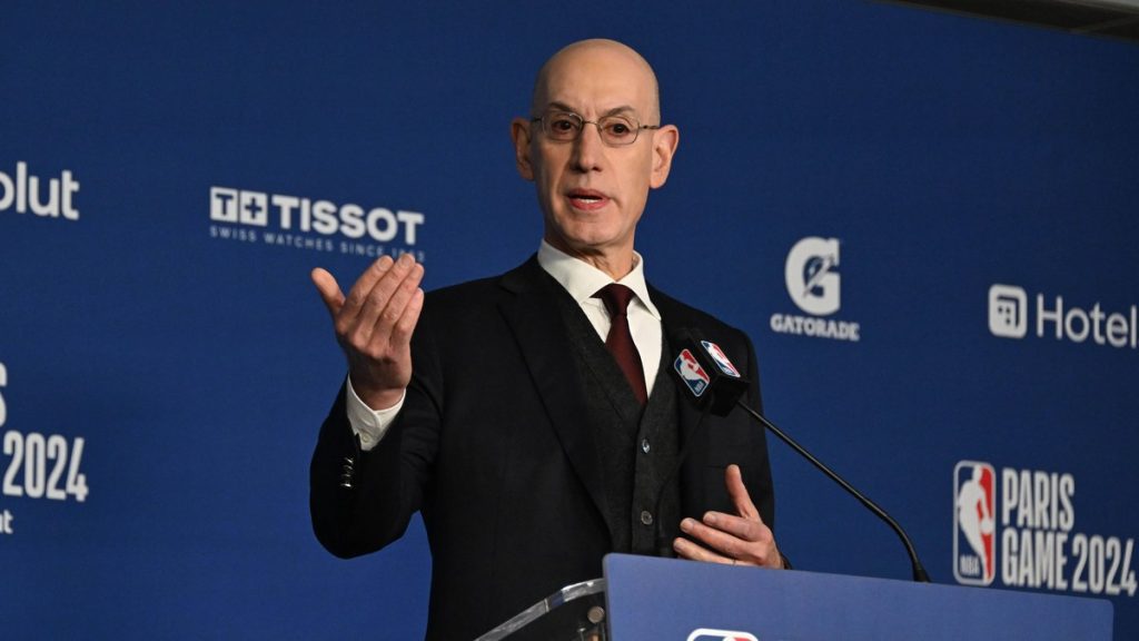 Adam Silver gesticula con la mano derecha tras el atril durante una rueda de prensa, con el panel azul de la NBA al fondo