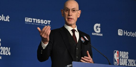 Adam Silver gesticula con la mano derecha tras el atril durante una rueda de prensa, con el panel azul de la NBA al fondo