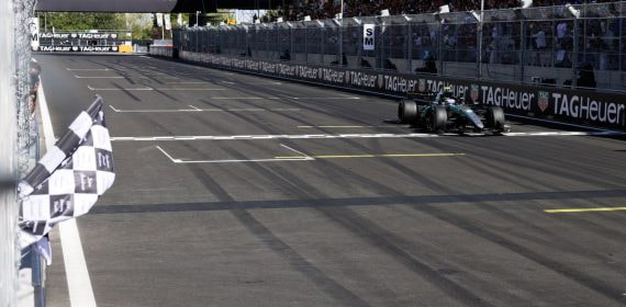 Un monoplaza cruza la línea de meta con la bandera a cuadros ondeando en primer plano
