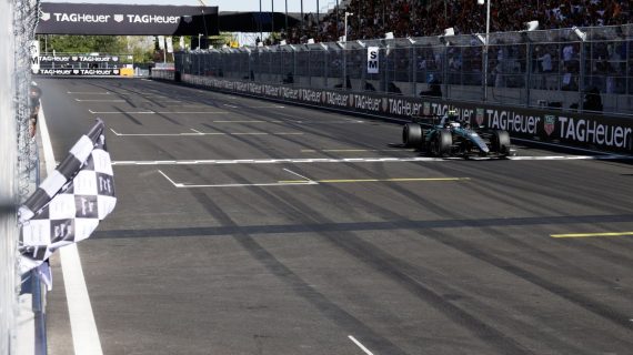 Un monoplaza cruza la línea de meta con la bandera a cuadros ondeando en primer plano