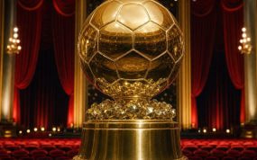 Trofeo dorado con forma de balón sobre un pedestal en el escenario de un teatro con cortinas de terciopelo rojo