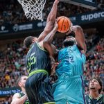 Un jugador del Barça de azul celeste lanza bajo el aro ante el tapón de un jugador del Joventut vestido de negro y verde