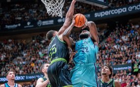 Un jugador del Barça de azul celeste lanza bajo el aro ante el tapón de un jugador del Joventut vestido de negro y verde