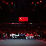 Las selecciones de Italia y China, alineadas en la pista bajo la bandera china durante los himnos en un pabellón en penumbra