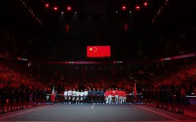Las selecciones de Italia y China, alineadas en la pista bajo la bandera china durante los himnos en un pabellón en penumbra