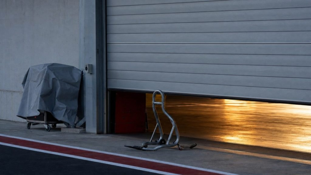 Box de competición cerrado con un caballete de moto vacío y la persiana medio bajada