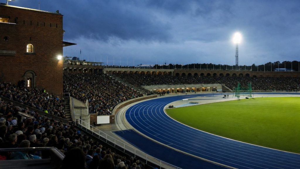 Vista desde la grada de la pista azul de un estadio de atletismo iluminado al anochecer