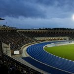 Vista desde la grada de la pista azul de un estadio de atletismo iluminado al anochecer