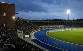Vista desde la grada de la pista azul de un estadio de atletismo iluminado al anochecer
