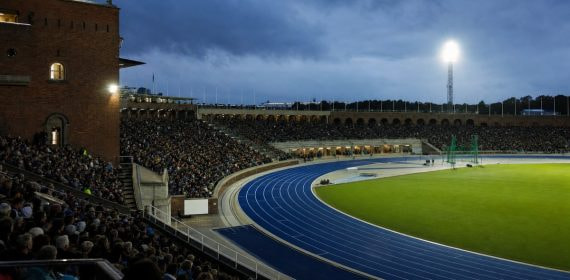 Vista desde la grada de la pista azul de un estadio de atletismo iluminado al anochecer