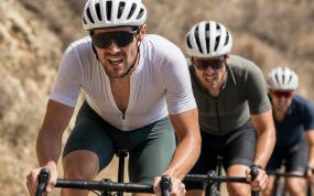 Tres ciclistas atacan de frente una rampa en una carretera de sierra bajo el sol