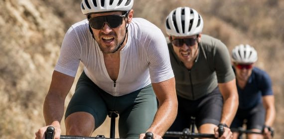 Tres ciclistas atacan de frente una rampa en una carretera de sierra bajo el sol