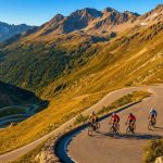Un grupo de ciclistas asciende una curva de herradura de un puerto de montaña bajo la luz de la tarde