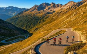 Un grupo de ciclistas asciende una curva de herradura de un puerto de montaña bajo la luz de la tarde