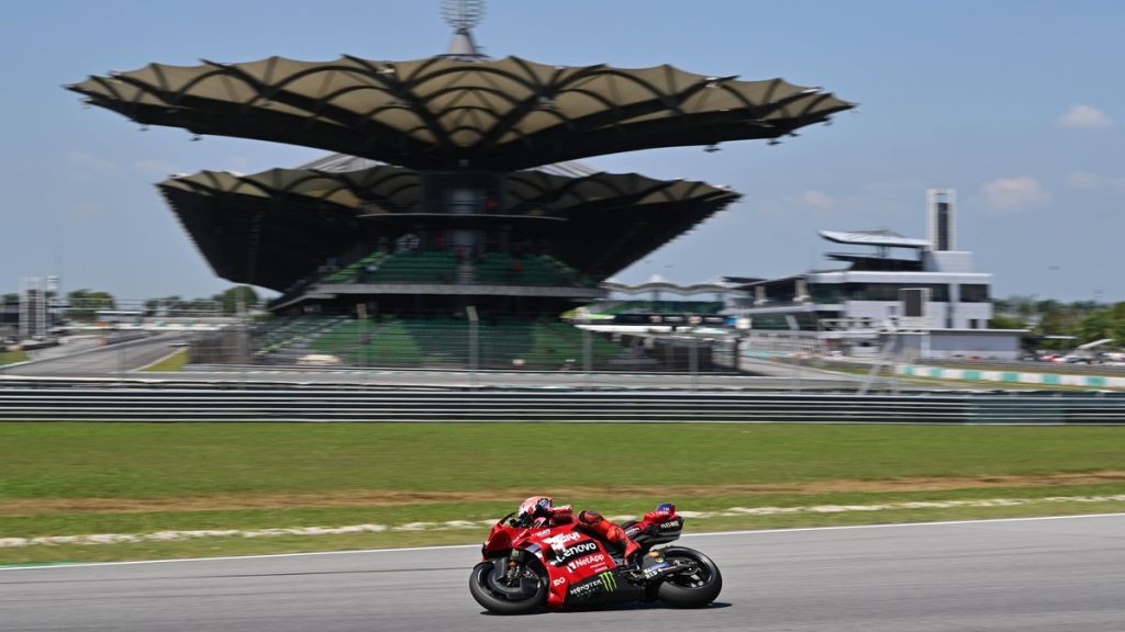 Una moto roja de Ducati rueda por la recta del circuito de Sepang con la tribuna principal y sus cubiertas en forma de hoja al fondo