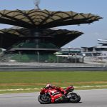 Una moto roja de Ducati rueda por la recta del circuito de Sepang con la tribuna principal y sus cubiertas en forma de hoja al fondo