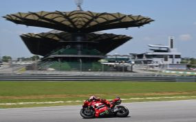 Una moto roja de Ducati rueda por la recta del circuito de Sepang con la tribuna principal y sus cubiertas en forma de hoja al fondo