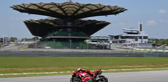 Una moto roja de Ducati rueda por la recta del circuito de Sepang con la tribuna principal y sus cubiertas en forma de hoja al fondo
