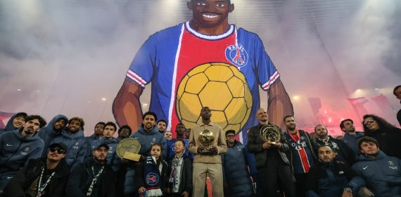 Ousmane Dembélé y Luis Enrique posan en el Parque de los Príncipes con sus respectivos trofeos delante de un tifo donde aparece el atacante francés con el Balón de Oro conseguido en 2025.