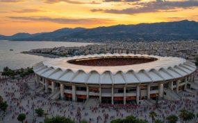 Estadio mediterráneo con cubierta blanca en forma de concha al atardecer, con aficionados camino de la entrada
