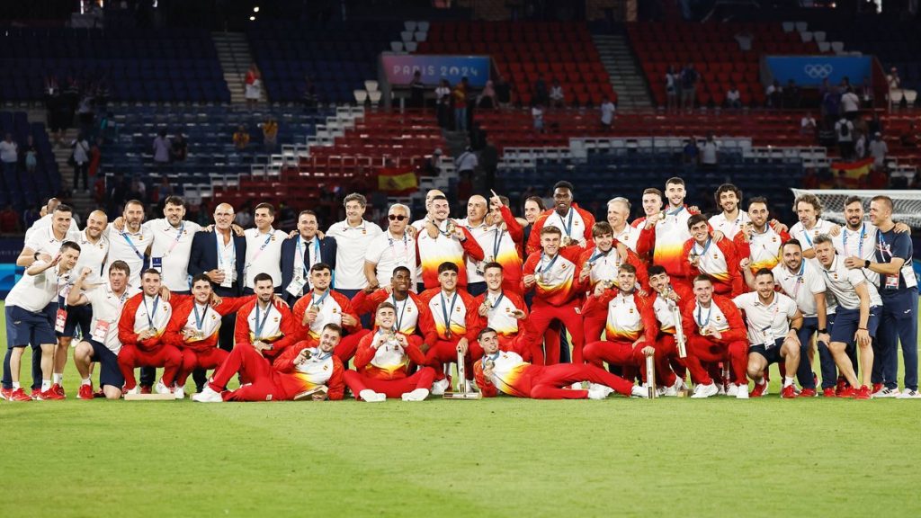 Los jugadores y el cuerpo técnico de la selección española posan con las medallas de oro sobre el césped de un estadio
