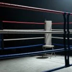 Esquina vacía de un ring de boxeo con las cuerdas en primer plano bajo un foco cenital