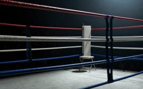 Esquina vacía de un ring de boxeo con las cuerdas en primer plano bajo un foco cenital