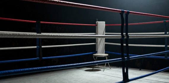Esquina vacía de un ring de boxeo con las cuerdas en primer plano bajo un foco cenital