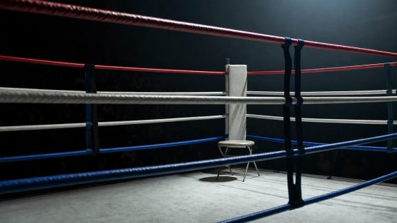Esquina vacía de un ring de boxeo con las cuerdas en primer plano bajo un foco cenital