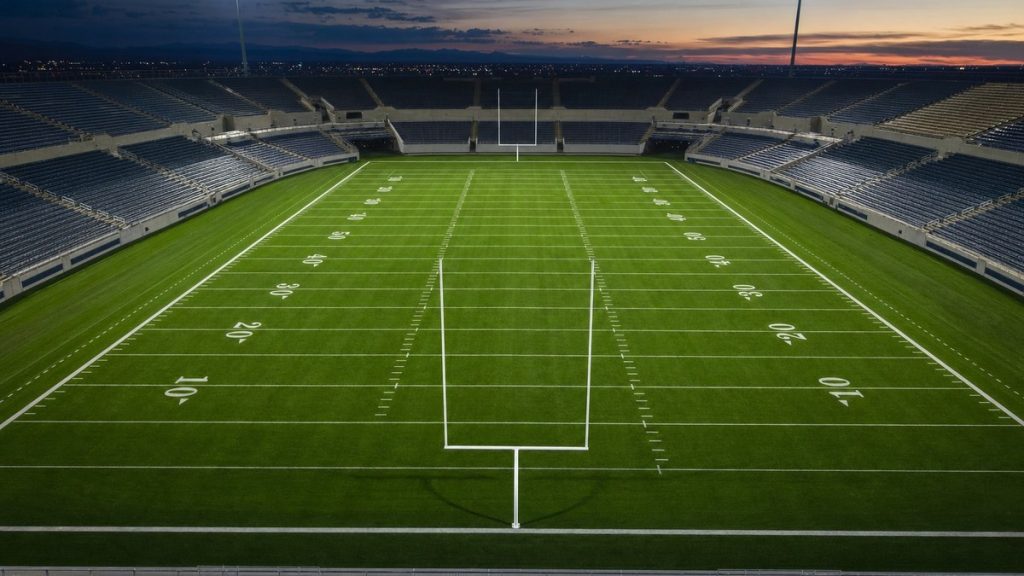 Campo de fútbol americano vacío con las líneas de yardas marcadas y los focos encendidos al anochecer