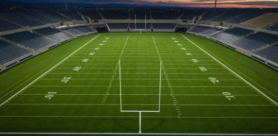 Campo de fútbol americano vacío con las líneas de yardas marcadas y los focos encendidos al anochecer