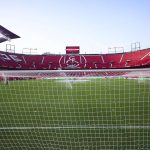 Vista del Estadio Ramón Sánchez-Pizjuán vacío desde detrás de la portería del Gol Sur, con las gradas rojas y el escudo del Sevilla al fondo