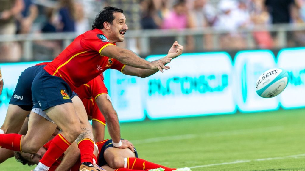 El medio melé Estanislao Bay, con la camiseta roja de España, suelta un pase desde el suelo junto a un ruck