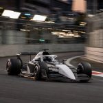 Un monoplaza de Fórmula 1 gris y blanco, sin patrocinadores, traza una curva de un circuito urbano al atardecer