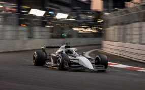 Un monoplaza de Fórmula 1 gris y blanco, sin patrocinadores, traza una curva de un circuito urbano al atardecer