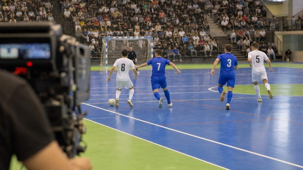 Una cámara de televisión enfoca una jugada de fútbol sala en un pabellón con las gradas llenas