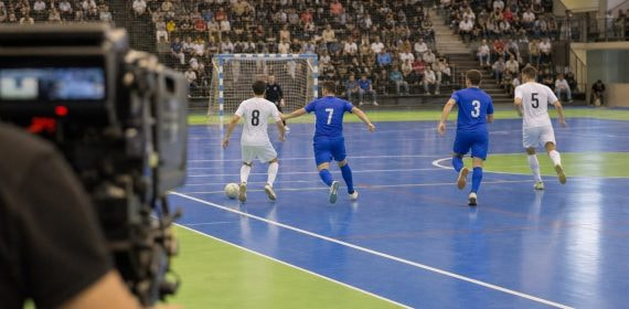 Una cámara de televisión enfoca una jugada de fútbol sala en un pabellón con las gradas llenas