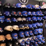 Una dependienta observa una pared entera de gorras de los New York Knicks en tonos azules y naranjas dentro de una tienda