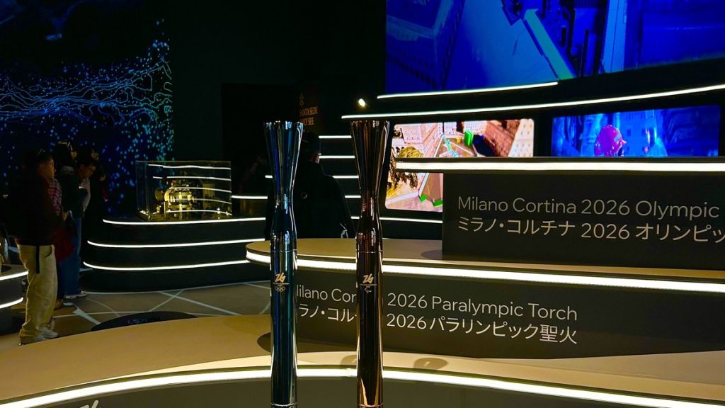Las antorchas olímpica y paralímpica de Milano-Cortina 2026, sobre una peana iluminada junto a los rótulos del evento