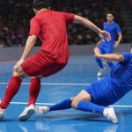 Un jugador de rojo protege el balón ante la entrada de un rival de azul en una pista de fútbol sala
