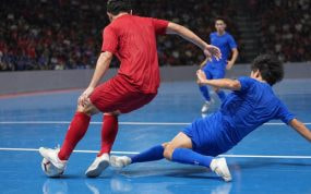 Un jugador de rojo protege el balón ante la entrada de un rival de azul en una pista de fútbol sala