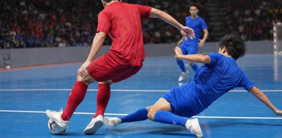 Un jugador de rojo protege el balón ante la entrada de un rival de azul en una pista de fútbol sala
