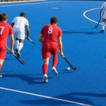 Jugadores de hockey hierba conducen la bola hacia el área sobre un campo de hierba artificial azul