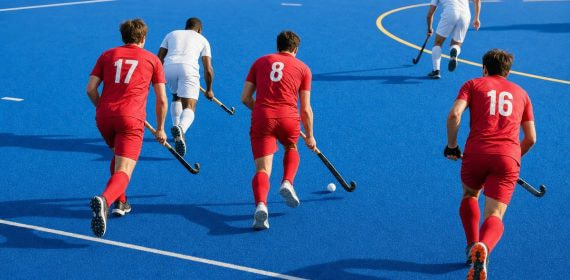 Jugadores de hockey hierba conducen la bola hacia el área sobre un campo de hierba artificial azul