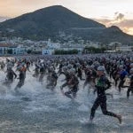 Cientos de triatletas con neopreno entrando al mar Mediterráneo al amanecer desde una playa ancha