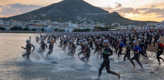 Cientos de triatletas con neopreno entrando al mar Mediterráneo al amanecer desde una playa ancha