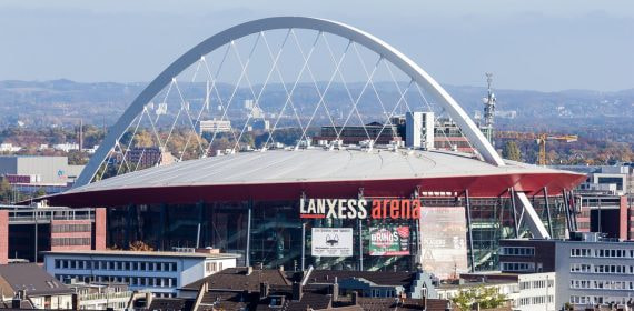 Vista exterior del Lanxess Arena de Colonia con su arco blanco sobre los tejados de la ciudad