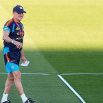 Luis de la Fuente, con gorra y ropa de entrenamiento de la selección, camina sonriente sobre el césped con un papel en la mano